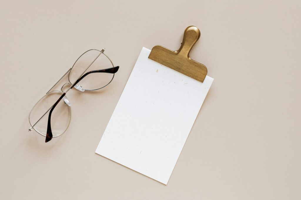 Elegant minimalist flat lay featuring eyeglasses and a clipboard on a beige background.